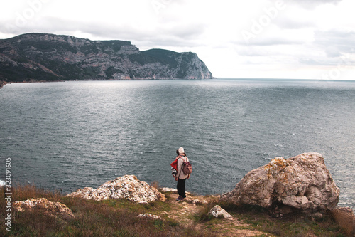 A young hipster woman stands on the edge of a cliff and looks into the distance. Winter travel to coastal countries.