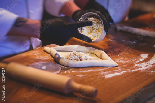 Process of cooking traditional adjarian georgian and armenian cuisine, hachapuri khachapuri with suluguni cheese and egg yolk on a wooden table with chief's hands in the background