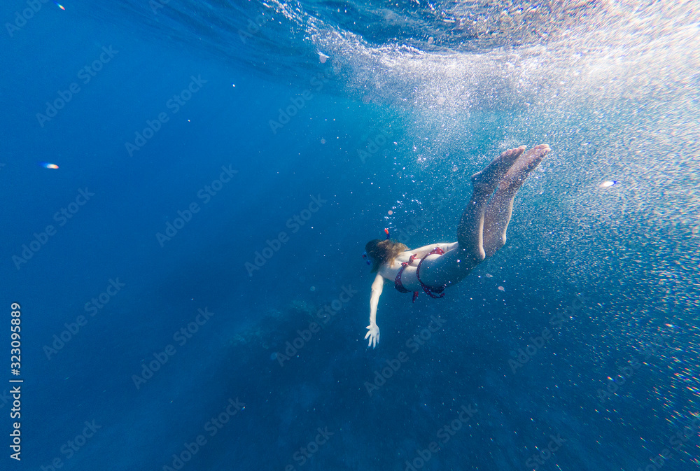 Girl with a mask and a snorkel dives into the sea with corals and fish