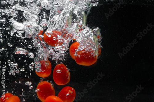Fototapeta Naklejka Na Ścianę i Meble -  Falling cherry tomatoes into the water, spray for design, freezing in motion