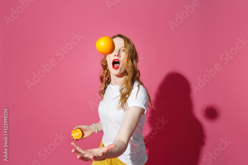 Fotografi Orange fruits, healthy eating, true emotions - a young blonde woman juggling oranges on pink background - diet, people and mood concept