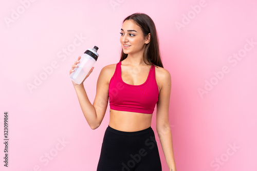 Young sport girl over isolated pink background with sports water bottle