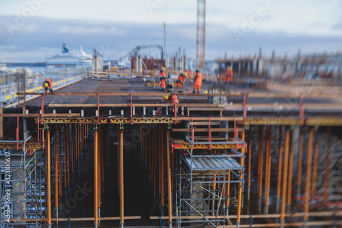 Process of apartment block construction, building site of multistoried residential house with underground car parking lot garage, with group of workers and engineers