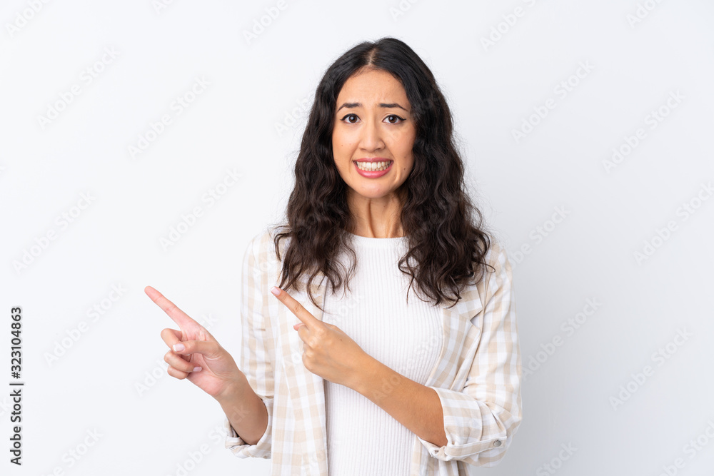 Mixed race woman over isolated white background frightened and pointing to the side Mixed race woman over isolated white background frightened and pointing to the side