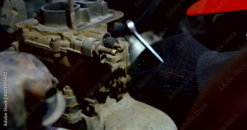 close-up of a man's hand in a black glove and with a wrench. unscrews the nut on the engine motor, then remove the gasket. dark key close-up of a man's hand in a black glove and with a wrench. unscrews the nut on the engine motor, then remove the gasket. dark key