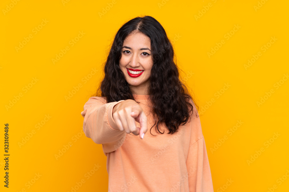 Spanish Chinese woman over isolated yellow background points finger at you with a confident expression Spanish Chinese woman over isolated yellow background points finger at you with a confident expression