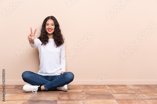 Young woman sitting on the floor smiling and showing victory sign