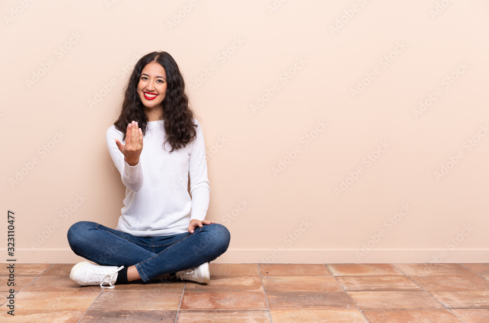Young woman sitting on the floor inviting to come with hand. Happy that you came Young woman sitting on the floor inviting to come with hand. Happy that you came
