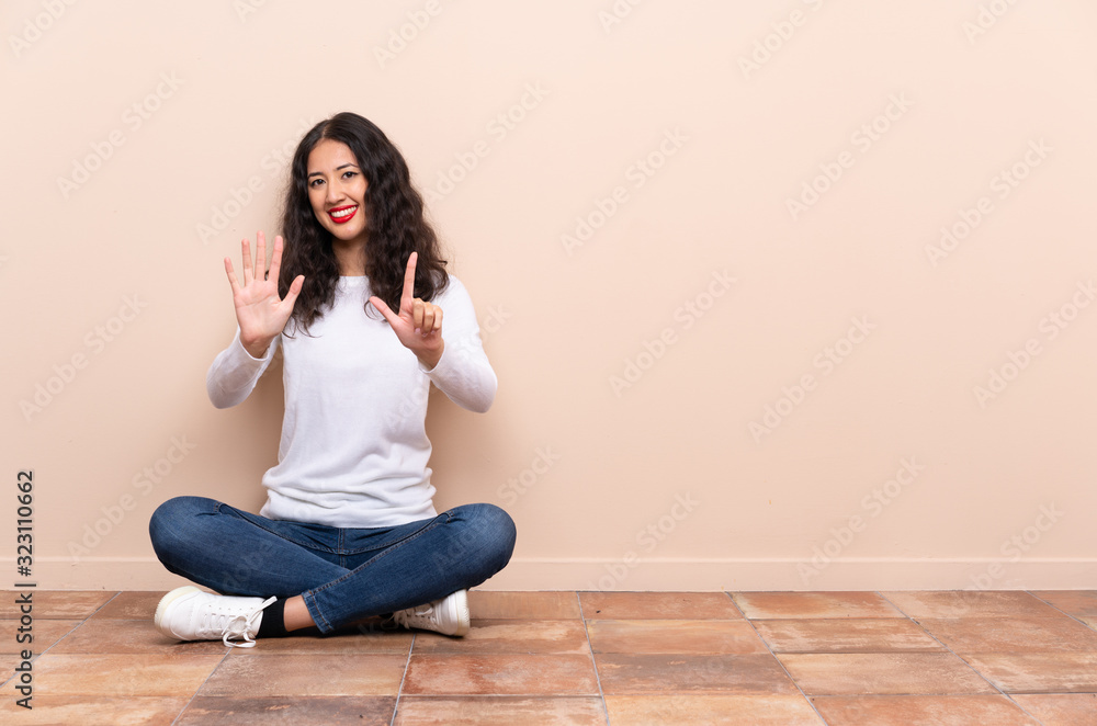Young woman sitting on the floor counting seven with fingers Young woman sitting on the floor counting seven with fingers