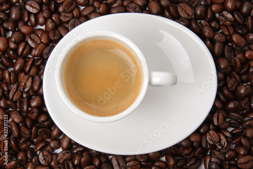 Cup of black coffee on coffee beans background. Hot aromatic americano or espresso cup on saucer. Top view.
