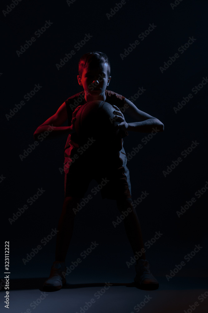 Kid playing basketball isolated on black background in mixed light