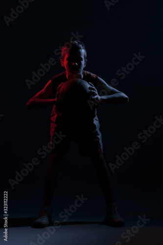 Kid playing basketball isolated on black background in mixed light