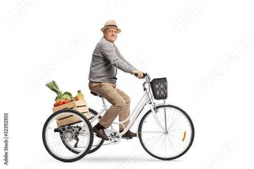 Elderly man riding a crate with fruits and vegetables on a tricycle