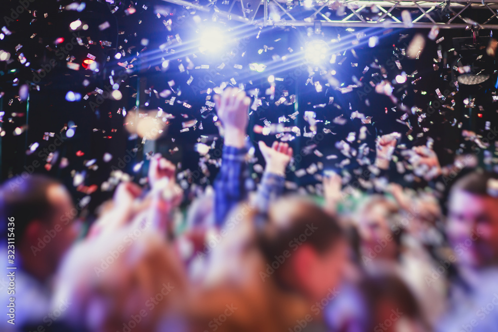 Colourful confetti explosion fired on dance floor air during a concert festival, crowded concert hall with scene stage lights, rock show performance, with people silhouette