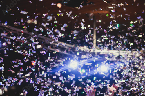 Colourful confetti explosion fired on dance floor air during a concert festival, crowded concert hall with scene stage lights, rock show performance, with people silhouette © tsuguliev