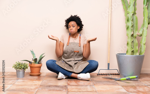 Gardener woman sitting on the floor having doubts while raising hands