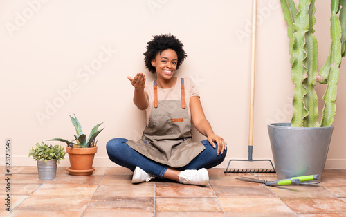 Gardener woman sitting on the floor inviting to come with hand. Happy that you came