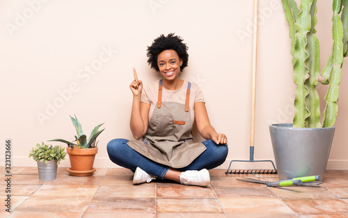 Gardener woman sitting on the floor showing and lifting a finger in sign of the best