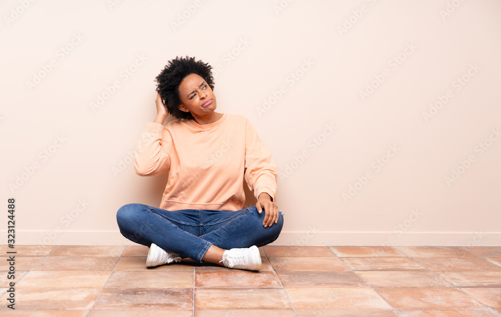 African american woman sitting on the floor having doubts while scratching head African american woman sitting on the floor having doubts while scratching head