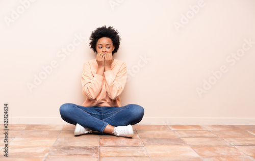 African american woman sitting on the floor nervous and scared putting hands to mouth