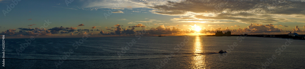 panorama, grateful sunrise over the ocean off the Bahama Islands with an orage sky, reflection on the sea and silhouettes of buildings in the background