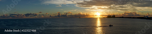 panorama, grateful sunrise over the ocean off the Bahama Islands with an orage sky, reflection on the sea and silhouettes of buildings in the background © Peter Jesche