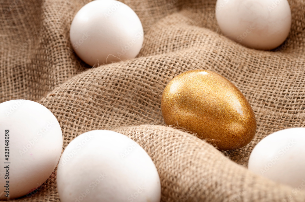 Metaphors for successful leadership and retirement investment concept with white eggs and one single gold egg on burlap sack background