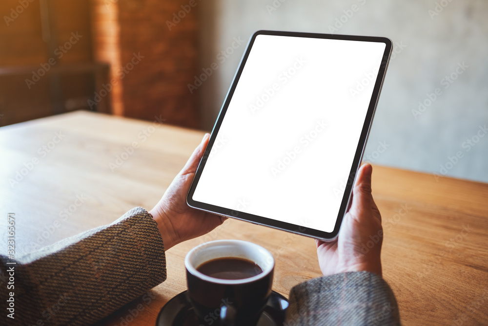 Mockup image of a woman holding black tablet pc with blank white screen with coffee cup on the table Mockup image of a woman holding black tablet pc with blank white screen with coffee cup on the table