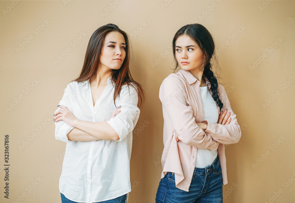 Young upset girls friends in casual offended at each other isolated on the beige background Young upset girls friends in casual offended at each other isolated on the beige background