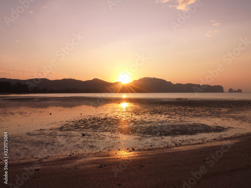 Exotic sunrise on a sandy beach with mountains in the background.