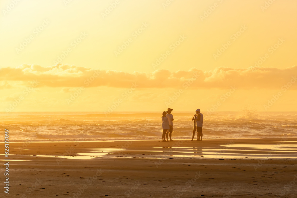 Fototapeta premium View of hazy North Piha beach in sunset light with four young people