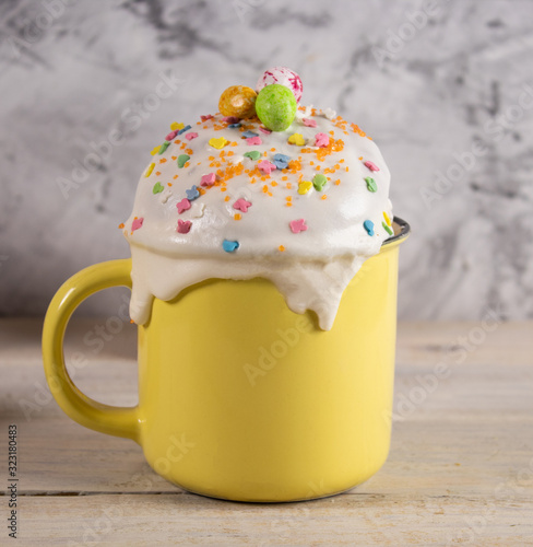 Cupcake for Easter in a mug with decoration and topping on a wooden table and a concrete background