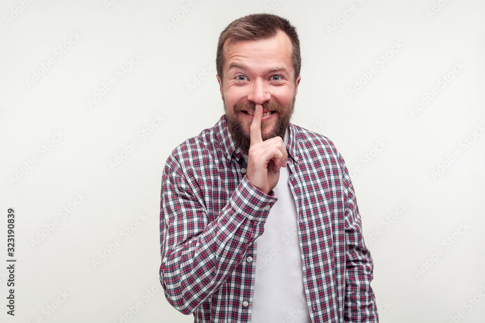 Be quiet! Portrait of cheerful bearded man in plaid shirt making hush silence gesture with finger on his lips, smiling asking to keep rumor in secret. indoor studio shot isolated on white background Be quiet! Portrait of cheerful bearded man in plaid shirt making hush silence gesture with finger on his lips, smiling asking to keep rumor in secret. indoor studio shot isolated on white background