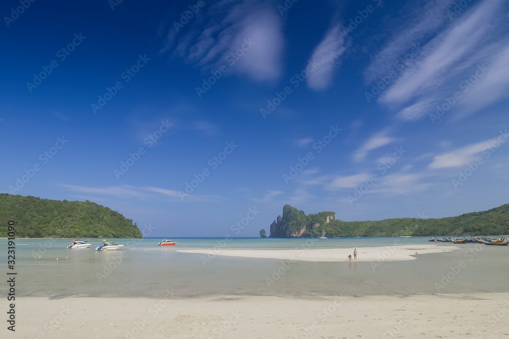 view seaside of speed boats, white sand beach and mountains with clouds moving in blue sky background, loh dalum beach, Phi Phi Don island, Krabi, southern of Thailand.