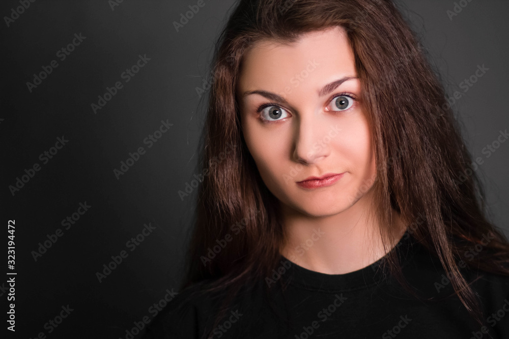 Fototapeta premium Portrait of a beautiful, young girl in black clothes with long hair. Studio photo, on a gray background. A model with clean skin.