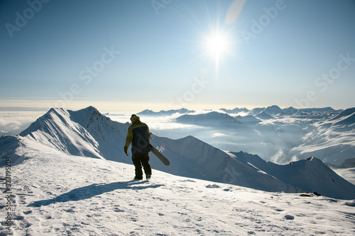 Male with snowboard walks on snowy mountain top