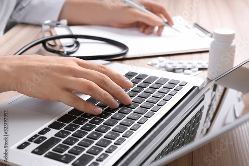 Doctor working with laptop at desk in office, closeup. Medical service
