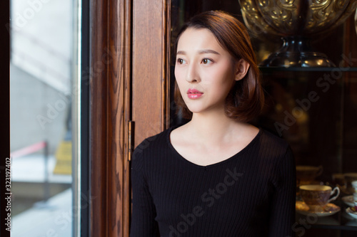 portrait of a young female wearing a black knitted sweater,standing by window. photo