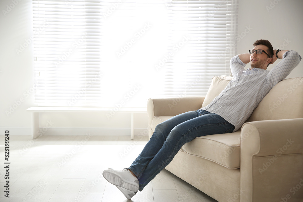 Young man relaxing on couch near window at home. Space for text