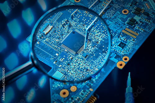Chip on the computer's motherboard close-up through a magnifying glass. Pinch the microchip with tweezers. The concept of repair of the motherboard.