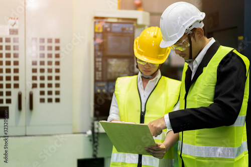 Worker or Male and Female Industrial Engineers in safety helmet Discuss New Project while looking Contract documents and funds on clipboard. They Work in Mold Plastic Industry Manufacturing Factory