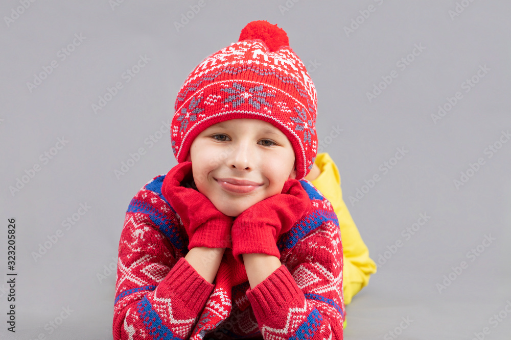 Joyful child in winter clothes on a gray background. Boy in a red knitted hat. Fashionable boy in the studio on a gray background. Joyful child in winter clothes on a gray background. Boy in a red knitted hat. Fashionable boy in the studio on a gray background.