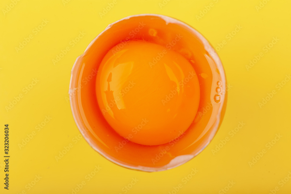 Egg Chicken eggs. Top view of one brown egg half broken, yellow round yolk. The concept of a healthy lifestyle, getting pure protein. Proper Breakfast. Preparing for Easter. Isolated on a yellow