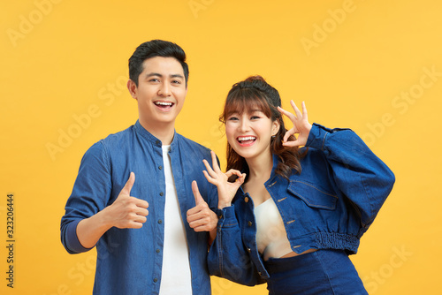 Foto Excited beautiful asian couple shows thumb up gesture agree to do something and collaborate against orange wall, did great job, show approval, like idea
