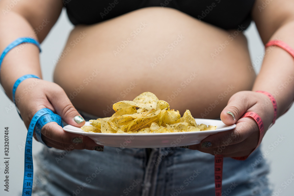 concept of Overweight woman eating junk food or Useful diet choices. Choose foods that are beneficial to the body. potato chip in obese fat young Asian woman and taking measurements of her hand. diet concept of Overweight woman eating junk food or Useful diet choices. Choose foods that are beneficial to the body. potato chip in obese fat young Asian woman and taking measurements of her hand. diet