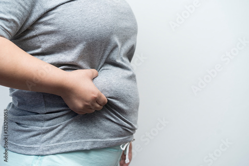 Concept fat, overweight, diet or cellulite and life and health care. side view female touching or holding fat and waist on gray background with copy space. Fat woman hand holding excessive belly fat photo