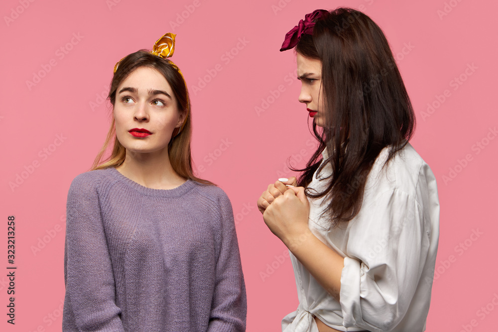 Stylish young female shaking fists, threatening her friend who is looking up with careless facial expression as if ignoring menace from her. Angry displeased woman expressing negative emotions Stylish young female shaking fists, threatening her friend who is looking up with careless facial expression as if ignoring menace from her. Angry displeased woman expressing negative emotions