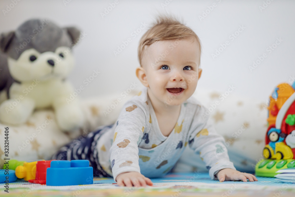 Adorable smiling playful blond little boy with beautiful blue eyes lying on stomach on the floor surrounded by toys. Adorable smiling playful blond little boy with beautiful blue eyes lying on stomach on the floor surrounded by toys.