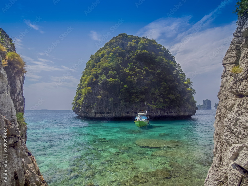 Naklejka premium view of a ship floating in blue-green sea with small island and blue sky background, Maya Bay, Phi Phi islands, Krabi, southern of Thailand.