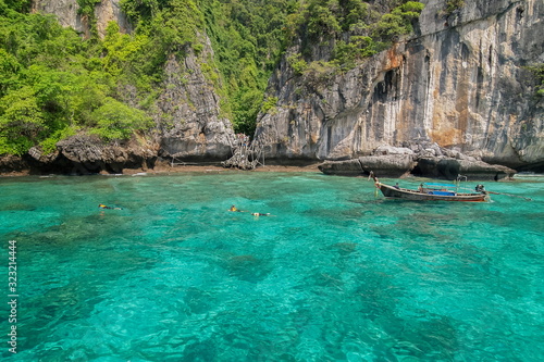 Sea view of a long-tail boat running in blue-green sea with Viking Cave and rock mountain in background, Loh samah bay, Phi Phi islands, Krabi, southern of Thailand.